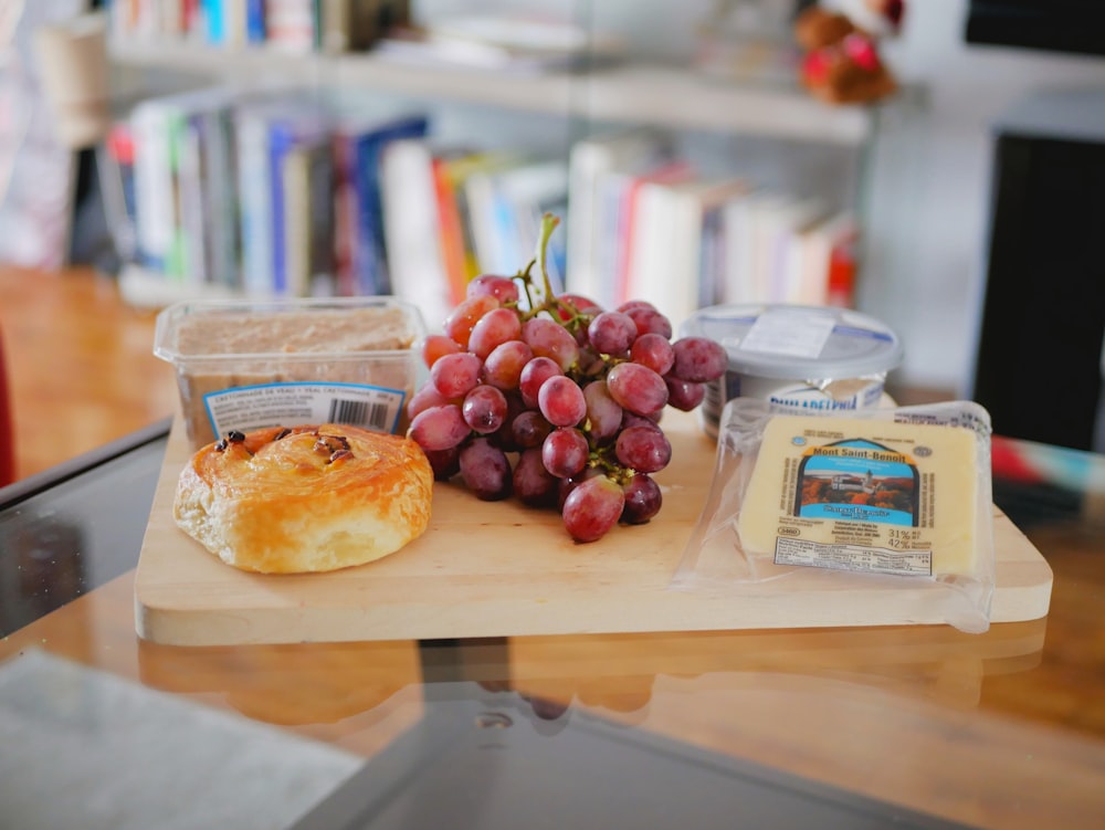 red grapes fruits near bread and other food on a wooden chopping board