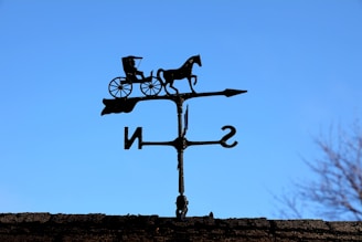 An elegant horse-shaped weathervane with intricate detailing, mounted on a farmhouse chimney.