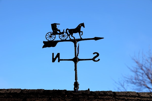 An elegant horse-shaped weathervane with intricate detailing, mounted on a farmhouse chimney.