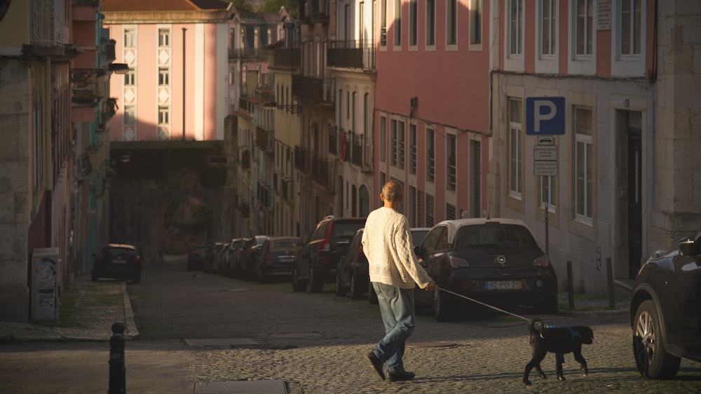 man walking a dog at the road near cars and buildings