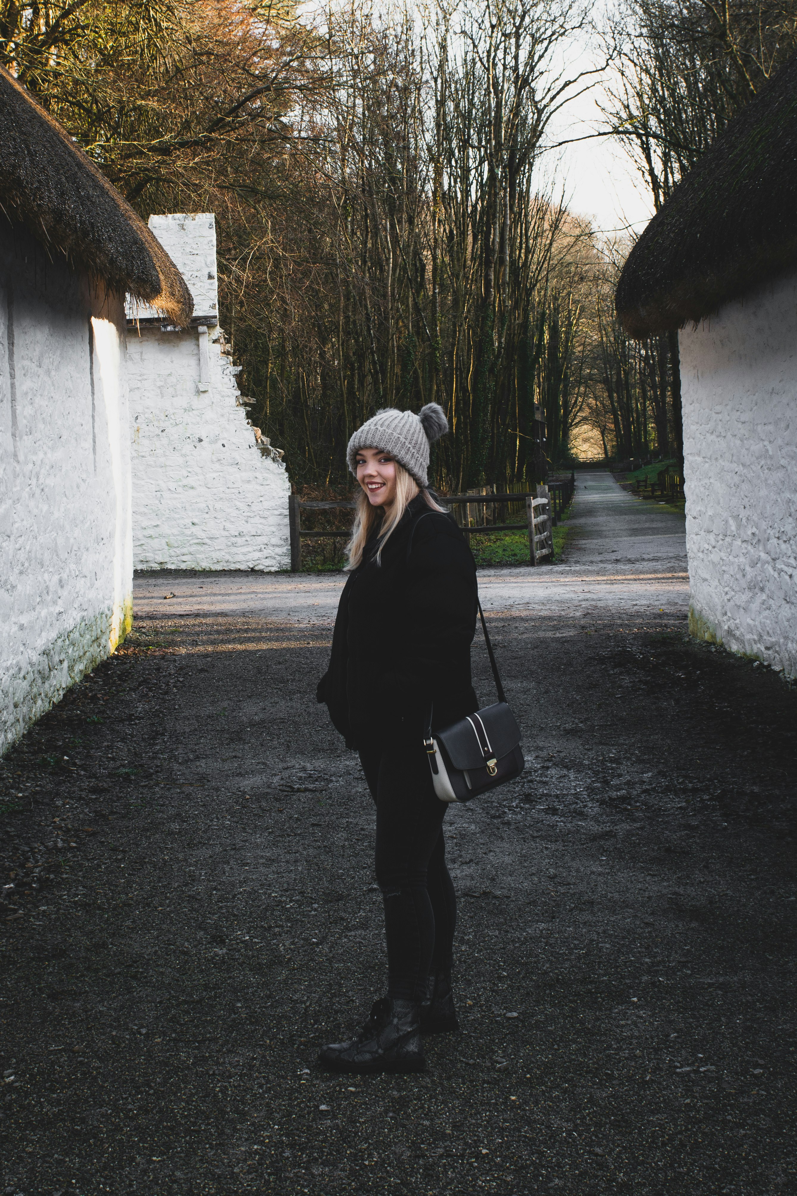 smiling woman wearing black jacket and pants carrying crossbody bag