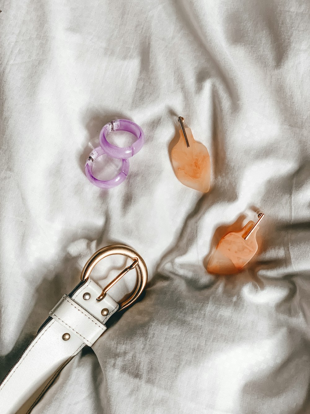 two pairs of beige and pink earrings beside white belt