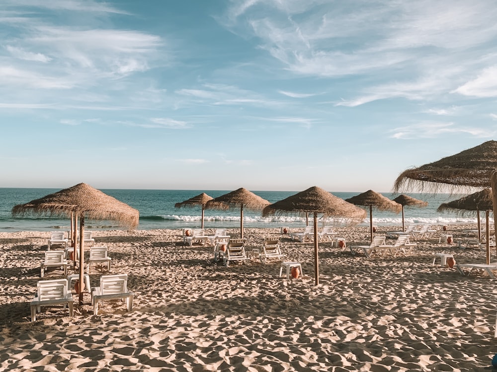 thatch parasols and lounge chairs on sand seashore during day