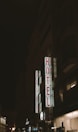 A nighttime scene featuring a tall building with illuminated signage displaying the words 'AVION' and 'HOTEL' in bright red letters vertically. The surrounding area is dimly lit, with other buildings partially visible in the background.