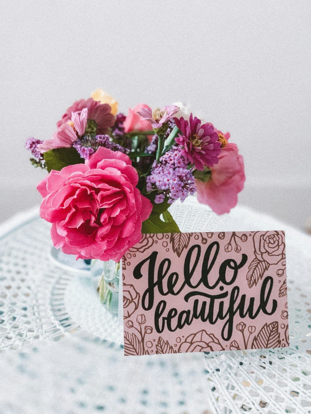 flowers in vase beside hello beautiful sign