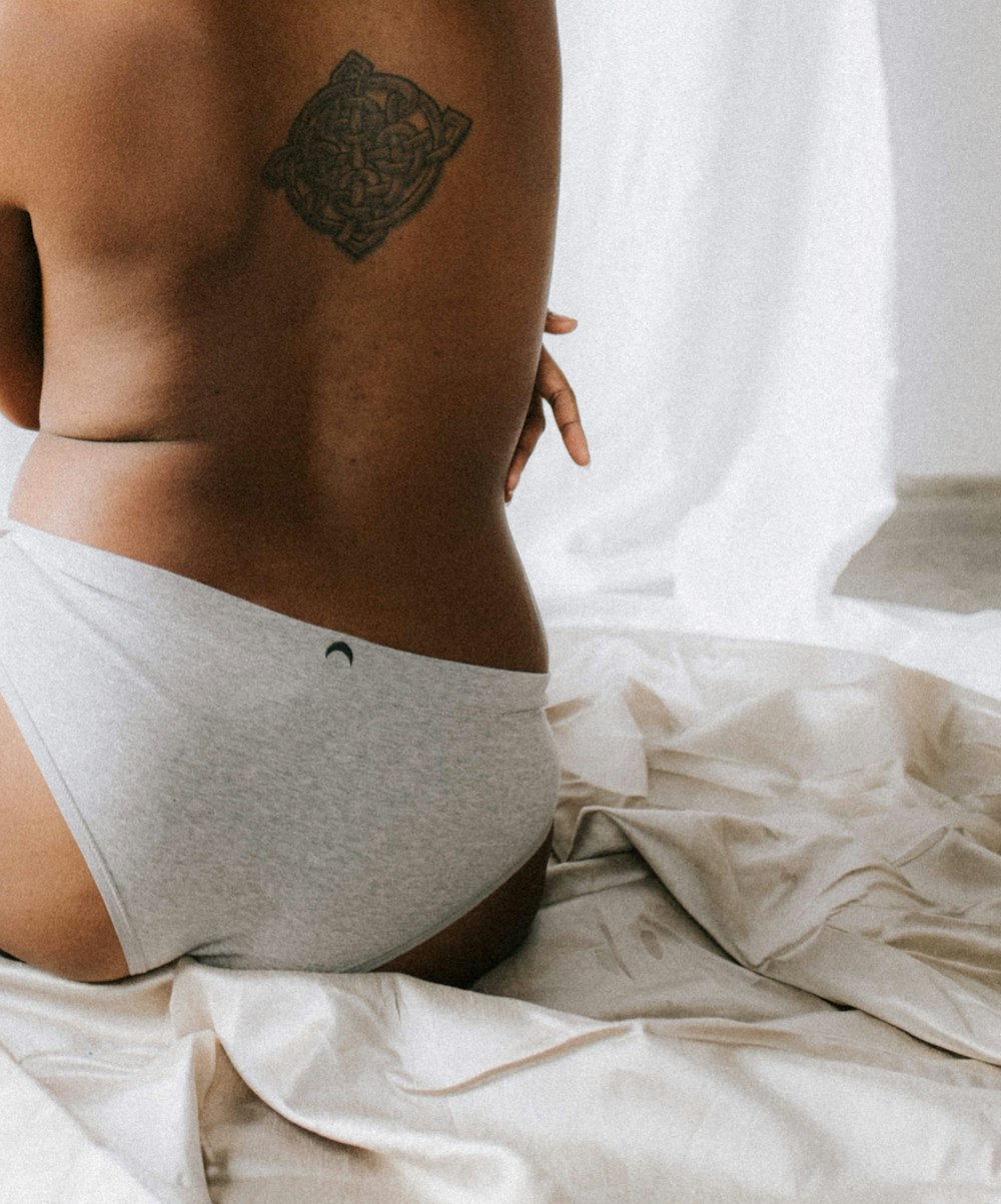 person wearing gray underwear with tribal back tattoo sitting on bed
