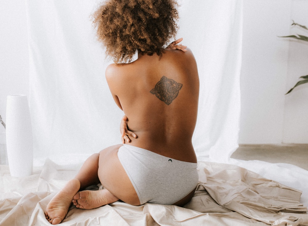 topless woman sitting on white textile