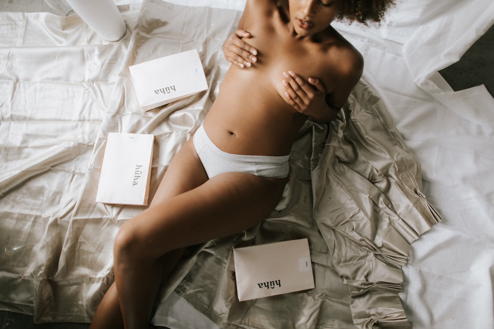 topless woman wearing white panty covering her breast while lying on bed