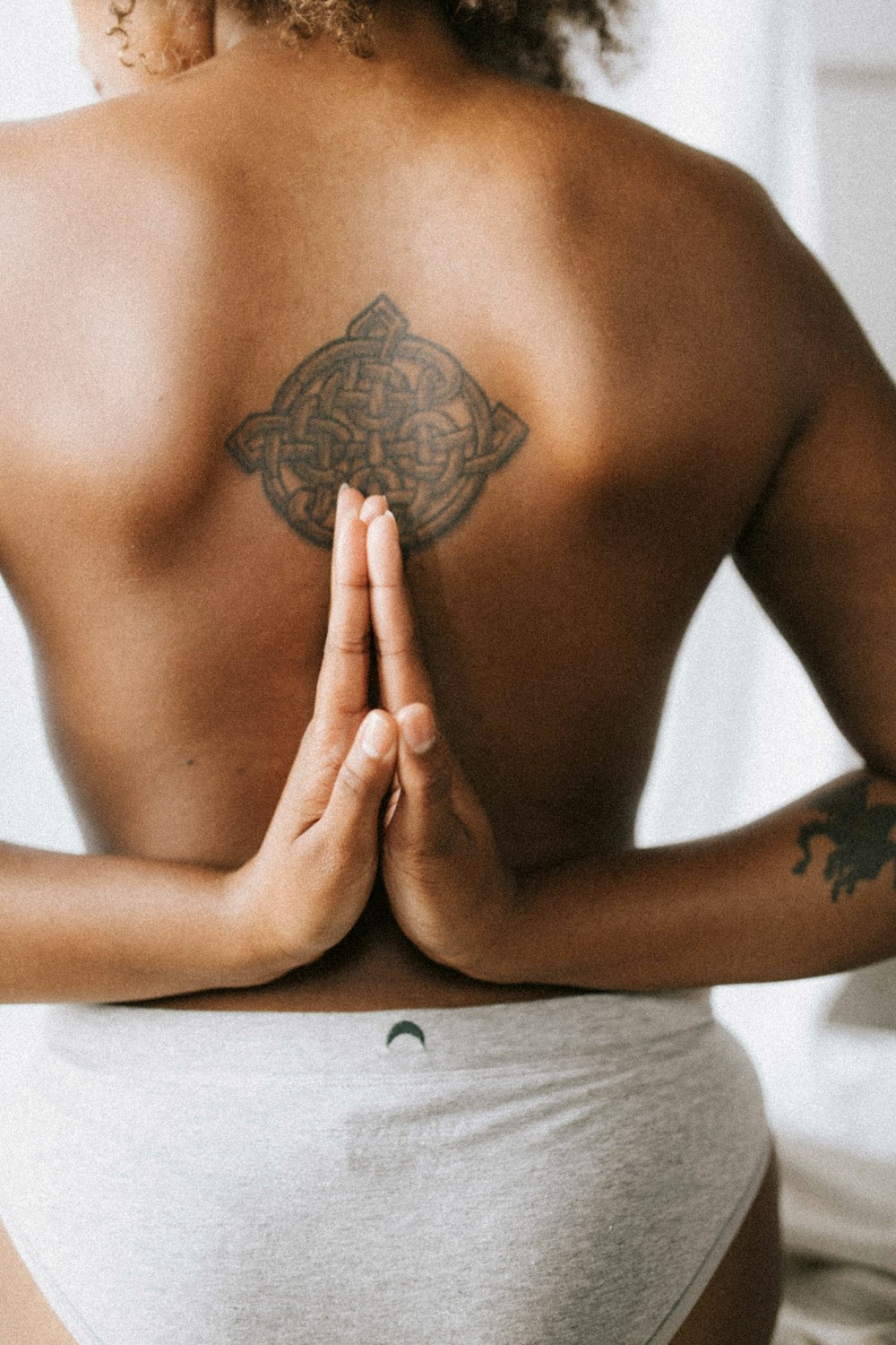 woman wearing white panty with tribal back tattoo putting putting hands on her back