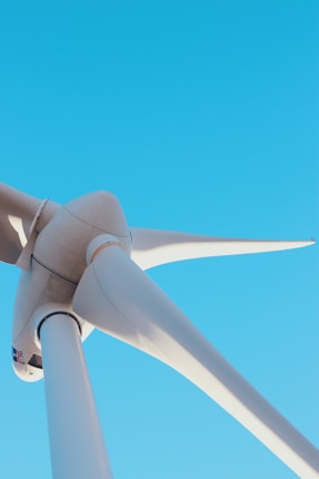 A close-up view of a large wind turbine against a clear blue sky. The image focuses on the turbine's blades and hub, capturing the sleek, aerodynamic design.