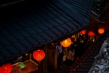 Travelers walking through a serene ancient alleyway lined with red lanterns.
