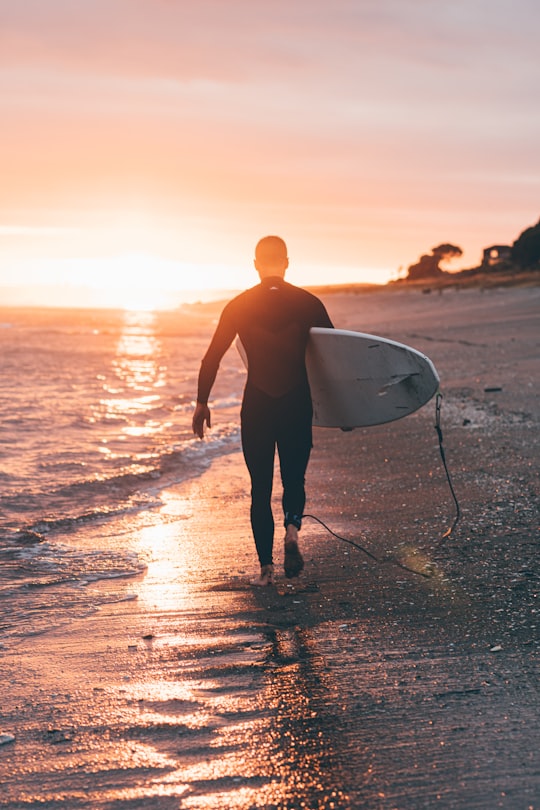 man holding white surfboard in Papamoa Beach New Zealand