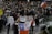 A large crowd gathers in a public square, participating in a protest. Many individuals hold signs with political and social messages, while some wave the Chilean flag. The atmosphere appears tense, with people engaged in animated discussions and chants. Several riot police officers in protective gear stand at the forefront, facing the protestors.