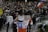 A large crowd gathers in a public square, participating in a protest. Many individuals hold signs with political and social messages, while some wave the Chilean flag. The atmosphere appears tense, with people engaged in animated discussions and chants. Several riot police officers in protective gear stand at the forefront, facing the protestors.