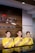 Three individuals are standing behind a reception desk, each wearing a yellow uniform. They are smiling and have their right hands placed over their chests. The background features a wooden wall with part of a logo and the word 'SEMARNG' visible.