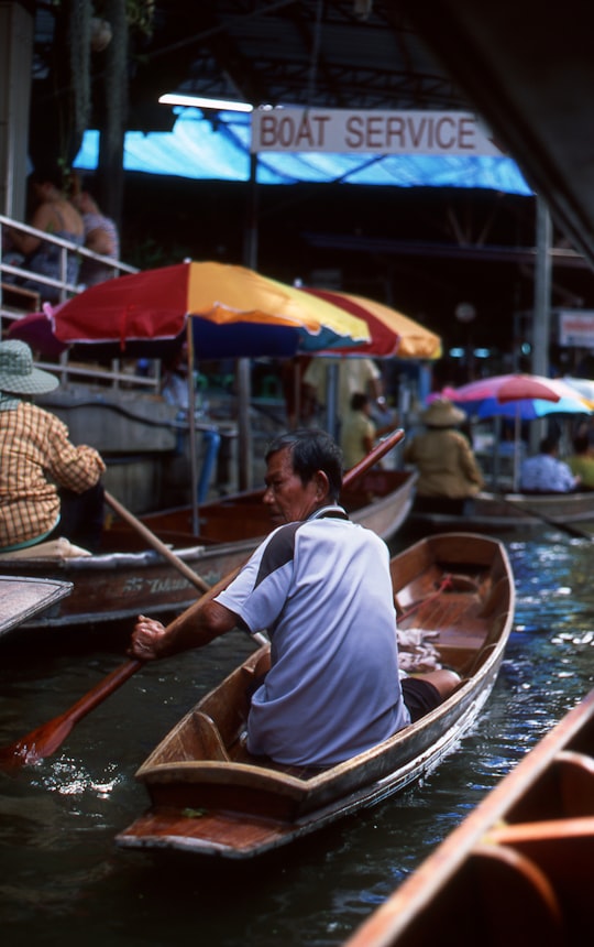 man wearing blue shirt riding on boat in Damnoen Saduak Thailand