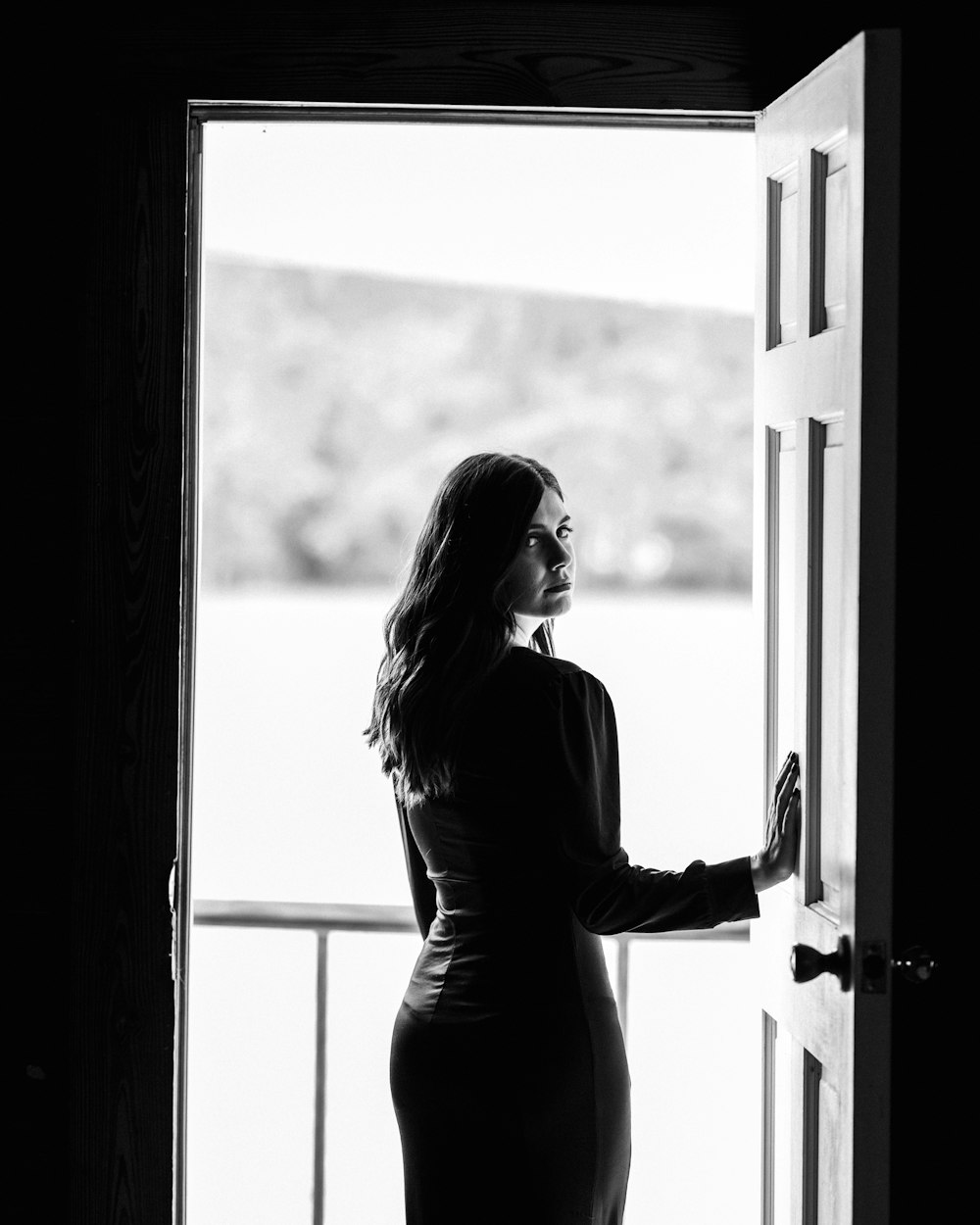 greyscale photography of woman standing beside door