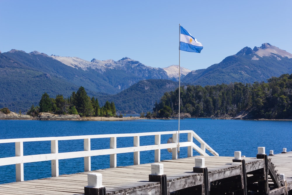 bandera blanca y azul en el muelle de madera cerca del cuerpo de agua durante el día