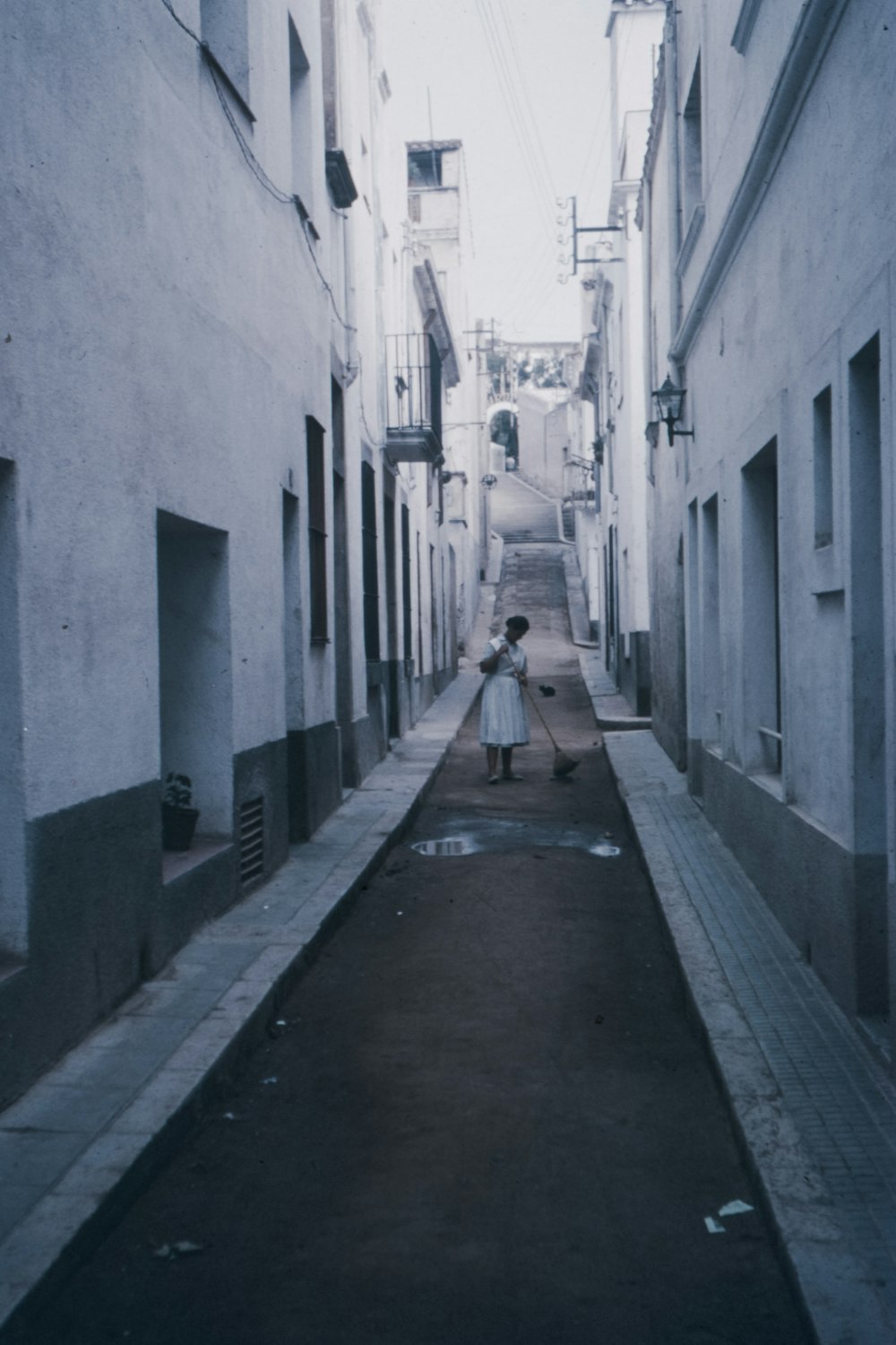 woman sweeping in the middle of the road between buildings