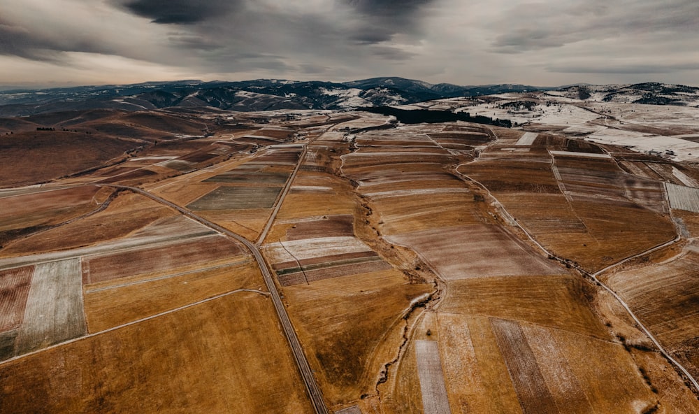 an aerial view of a field and mountains under a cloudy sky