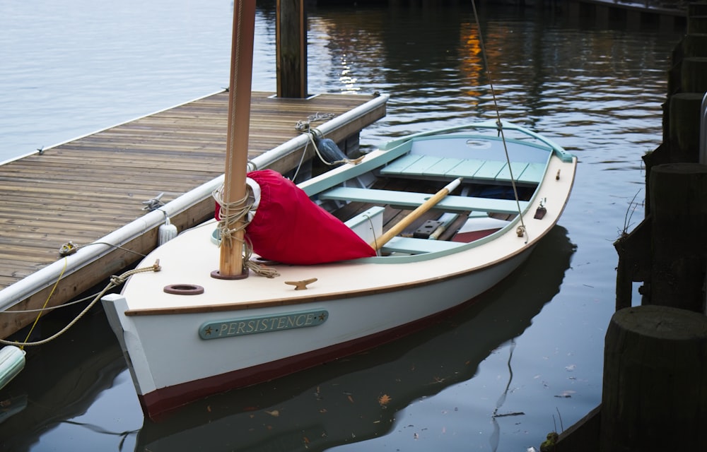 Weißes Boot auf ruhigem Gewässer neben braunem Dock während des Tages