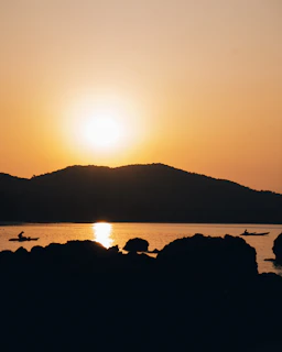 Sunset casting warm hues over the estuary with kayaks silhouetted against the sky.