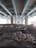 A large concrete structure, likely a highway or bridge, supported by multiple pillars extends overhead. The ground beneath is covered with rocks and debris. The lighting is dim, with some snow visible on the rocks.