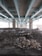 A large concrete structure, likely a highway or bridge, supported by multiple pillars extends overhead. The ground beneath is covered with rocks and debris. The lighting is dim, with some snow visible on the rocks.