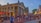 A bustling outdoor scene with numerous people walking or standing around a historic market building with columns. The building, called Quincy Market, has a classic architectural style. Red umbrellas and lights adorn an outdoor dining area where people are sitting. The street is paved with brick, adding a historic charm to the area. Signs for nearby businesses are visible, and trees and cityscape can be seen in the background.
