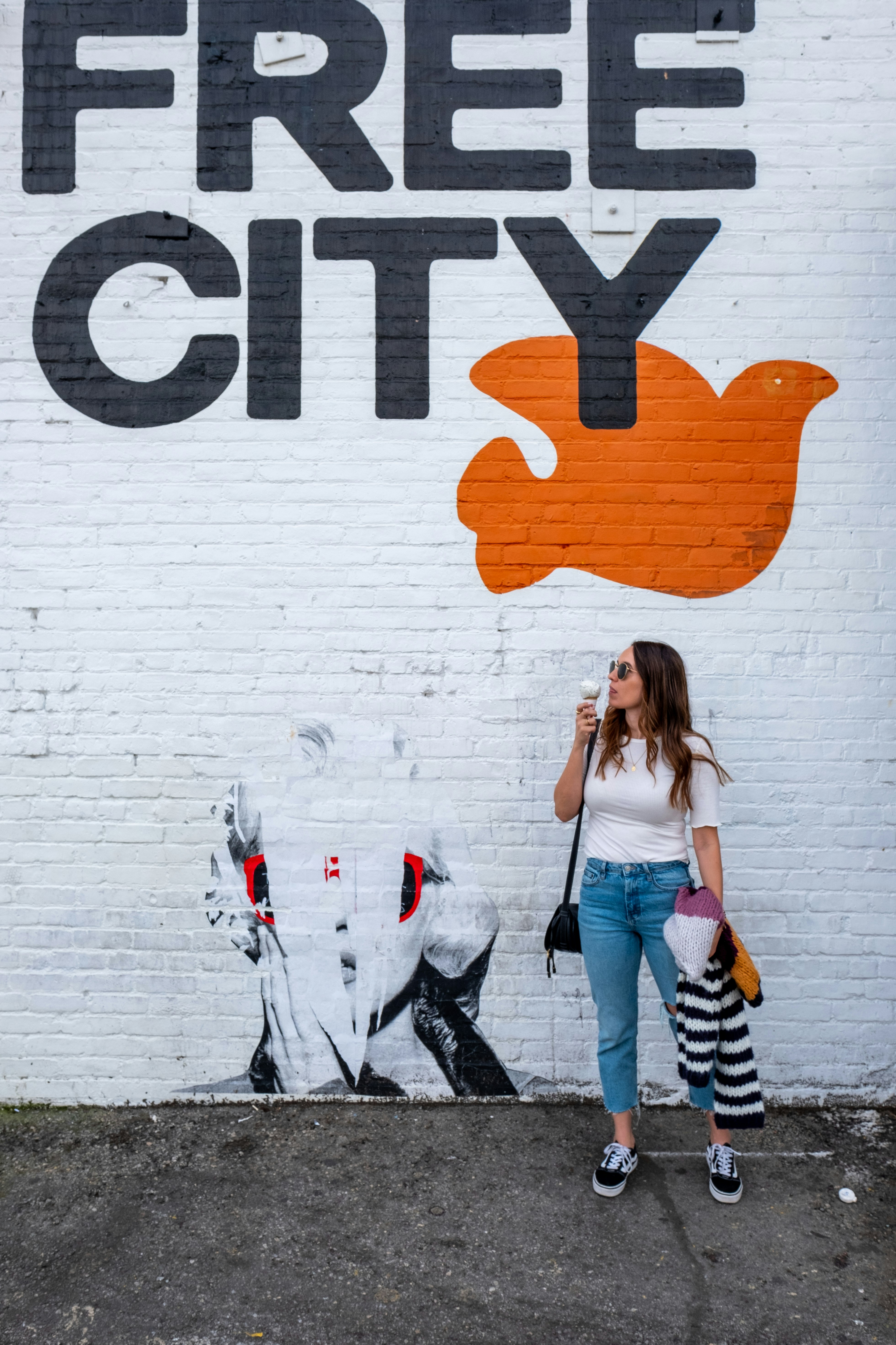 woman standing and holding ice cream beside wall with Free City sign