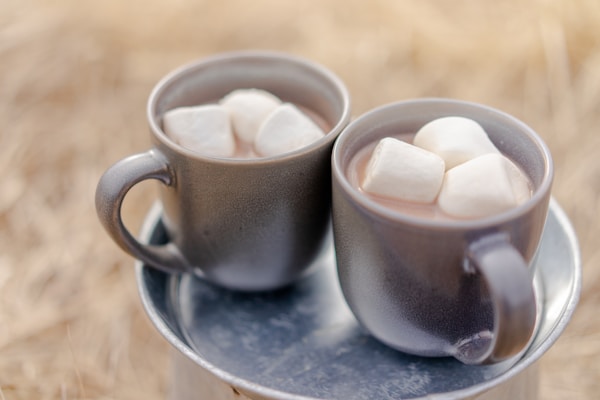 Two mugs of beverages and marshmallows
