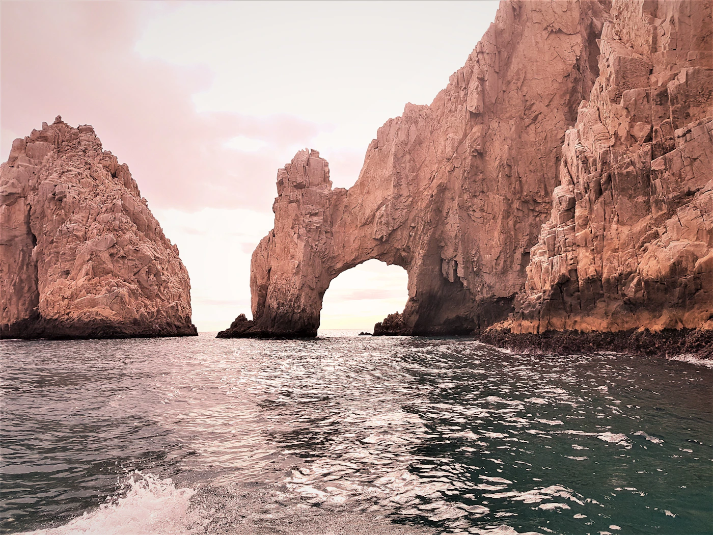 El Arco de Cabo San Lucas at dusk, the granite rock face turning deep amber and mauve in the last light as the sun drops toward the Pacific horizon