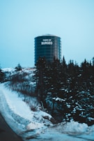 A large cylindrical water tower labeled 'Town of Burgeo' stands amidst a snowy landscape. Surrounding the tower are snow-covered trees, and the area has a cold, wintry atmosphere. The sky is overcast, adding to the chilly environment.
