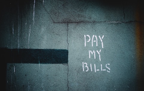 A weathered wall with a faded green texture features graffiti that reads 'PAY MY BILLS' in white paint. A dark horizontal line runs across the left side of the wall.