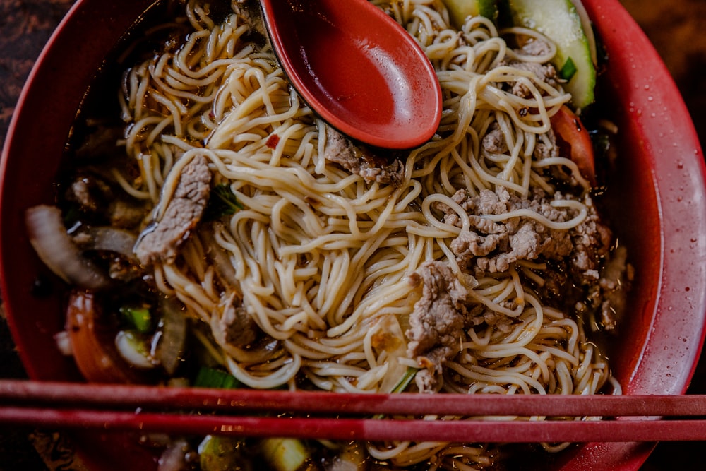 noodles with meat and spring onions in round red bowl