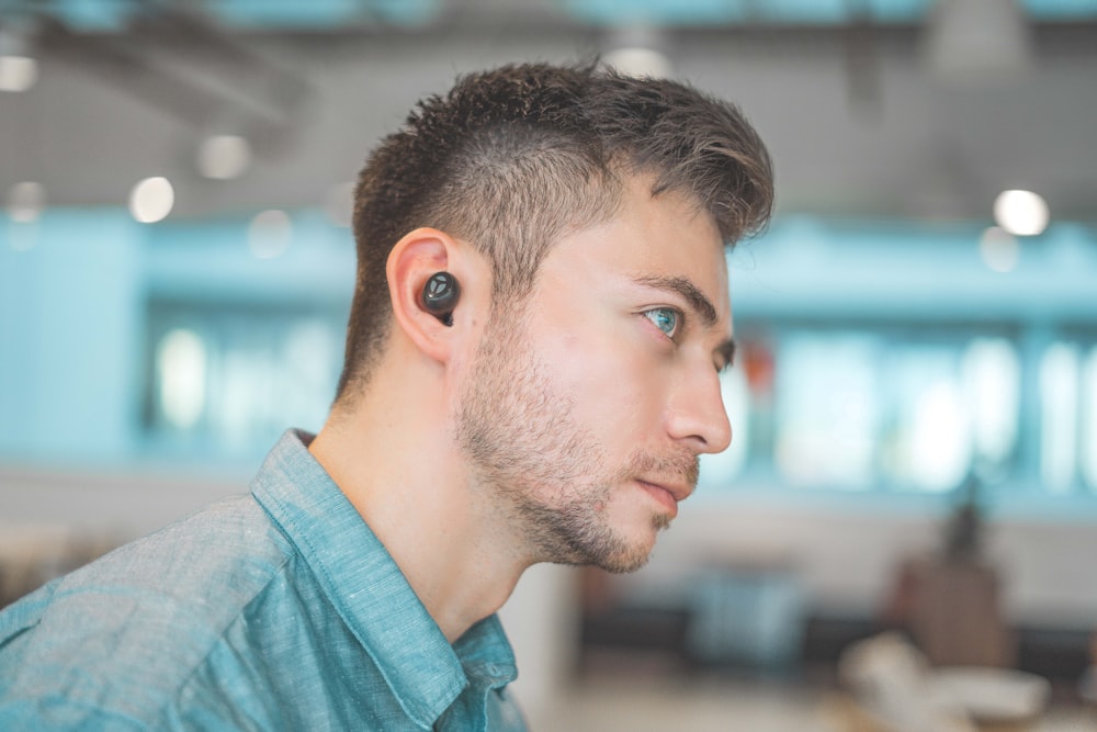 man wearing blue dress shirt with black Bluetooth earbuds