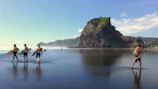 A group of surfers carrying their boards walking towards the water under a bright blue sky.