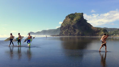 A group of surfers carrying their boards walking towards the water under a bright blue sky.