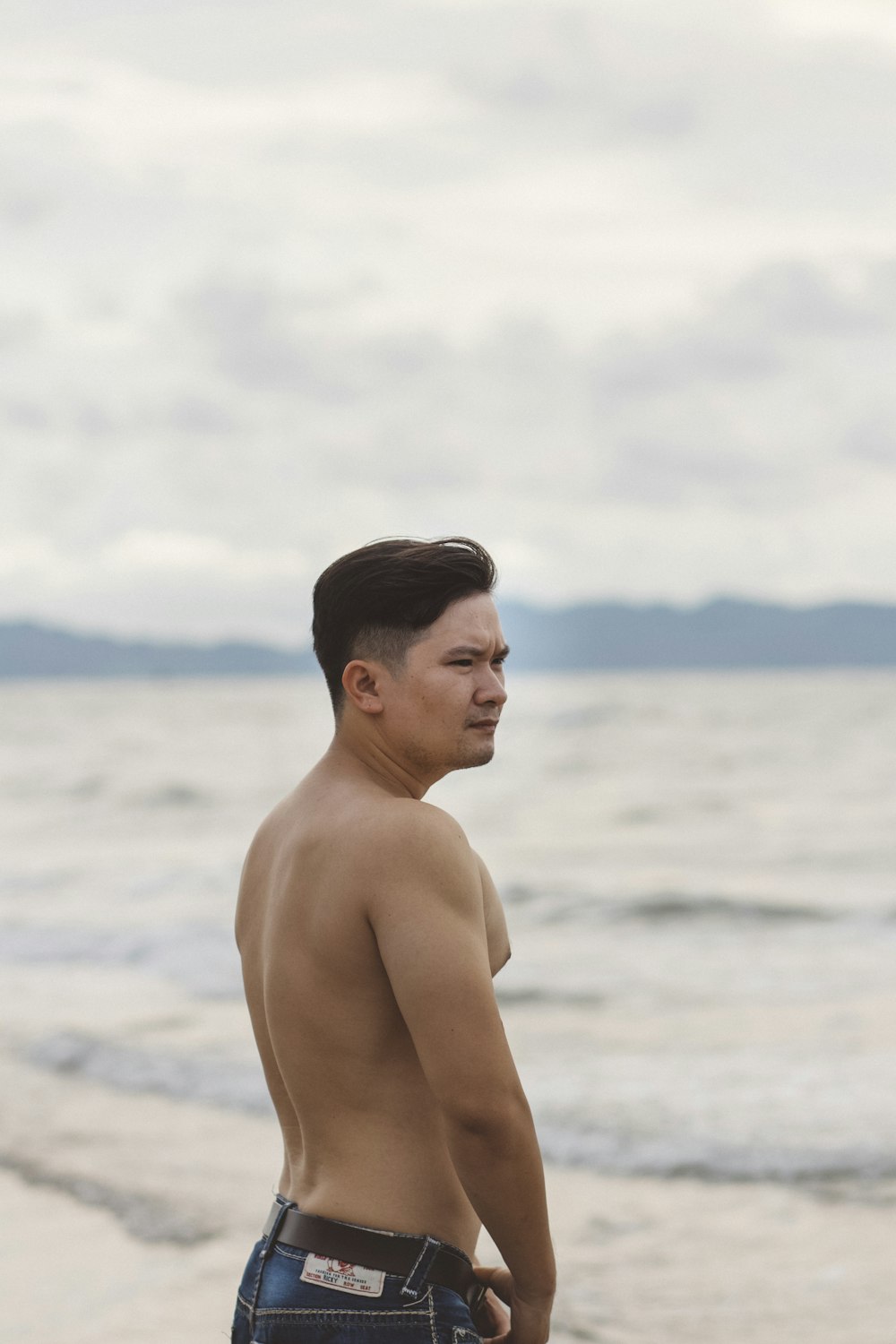 shallow focus photo of topless man standing near ocean