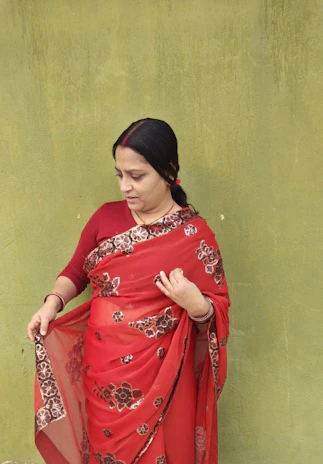 Classic Banarasi silk saree in rich red with intricate patterns, displayed on a traditional wooden hanger.