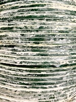 A close-up view of a stack of dark green tires covered in white dust or residue. The horizontal lines formed by the stacked tires create a pattern, and the surface texture appears rough and uneven.