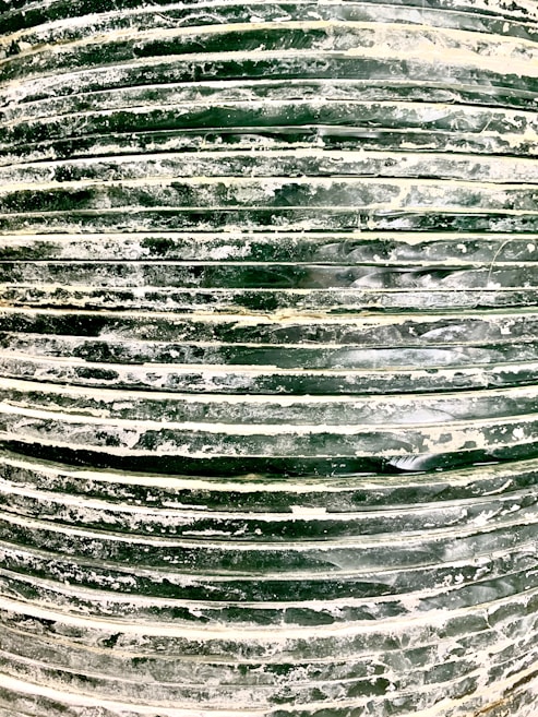 A close-up view of a stack of dark green tires covered in white dust or residue. The horizontal lines formed by the stacked tires create a pattern, and the surface texture appears rough and uneven.