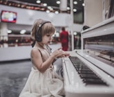 girl wearing headphones sitting in front of white piano