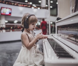girl wearing headphones sitting in front of white piano