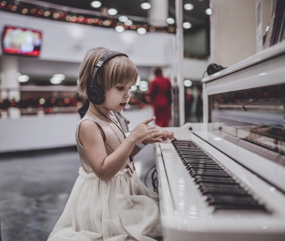 흰색 피아노 앞에 앉아 헤드폰을 착용 한 소녀