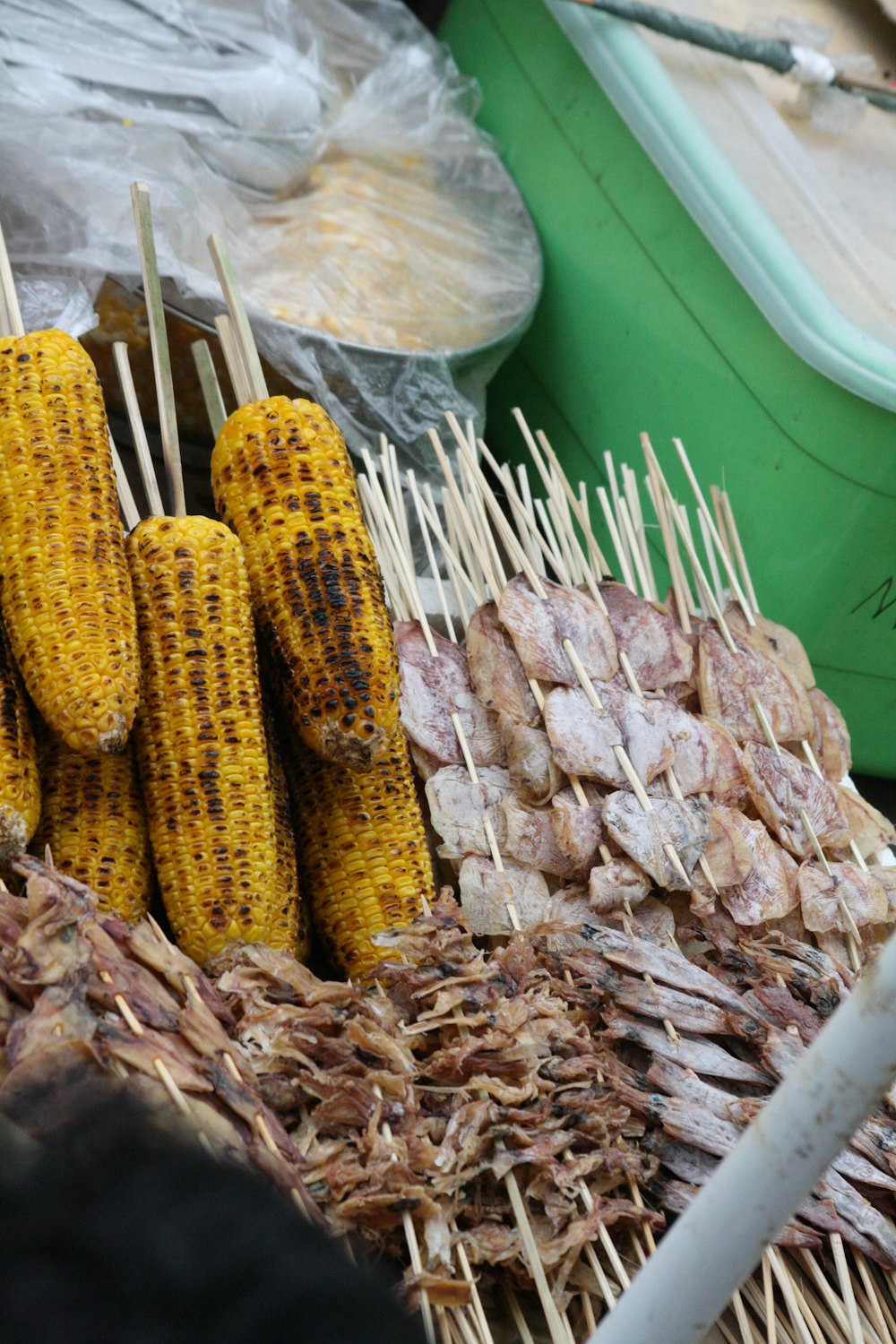 piles of barbecued corns on sticks beside meat slices on sticks