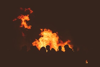 A group of friends dancing around a fire at sunset.
