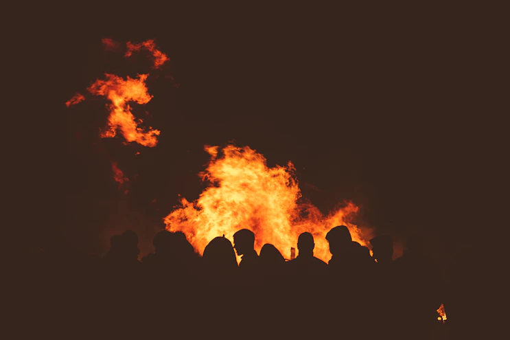 A vibrant group gathered around a glowing fire, hands raised in worship under a twilight sky.