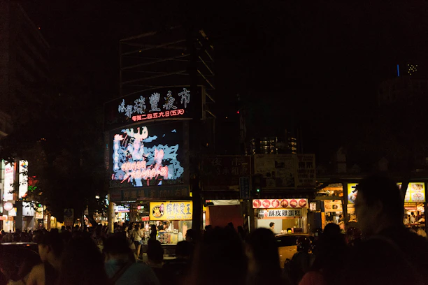 A large LED screen mounted on a storefront attracting a crowd during evening hours.