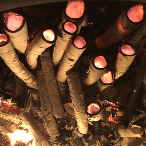 Several logs appear to be burning from the inside, creating a glowing effect from their hollow ends. The scene conveys a rustic and warm ambiance, with the logs arranged closely together.